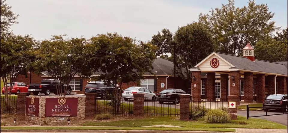 Brick one-story building with gated entrance, signage reading Royal Retreat, and nearby parked cars.