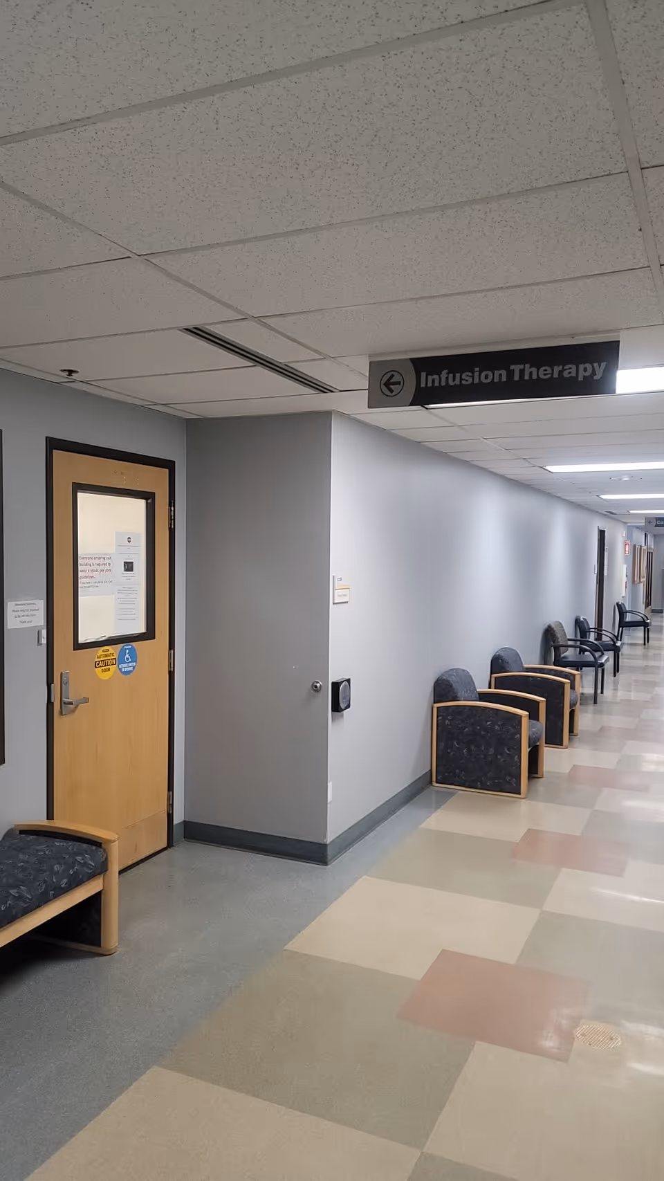 Long hospital corridor with infusion therapy sign and row of waiting chairs along the wall