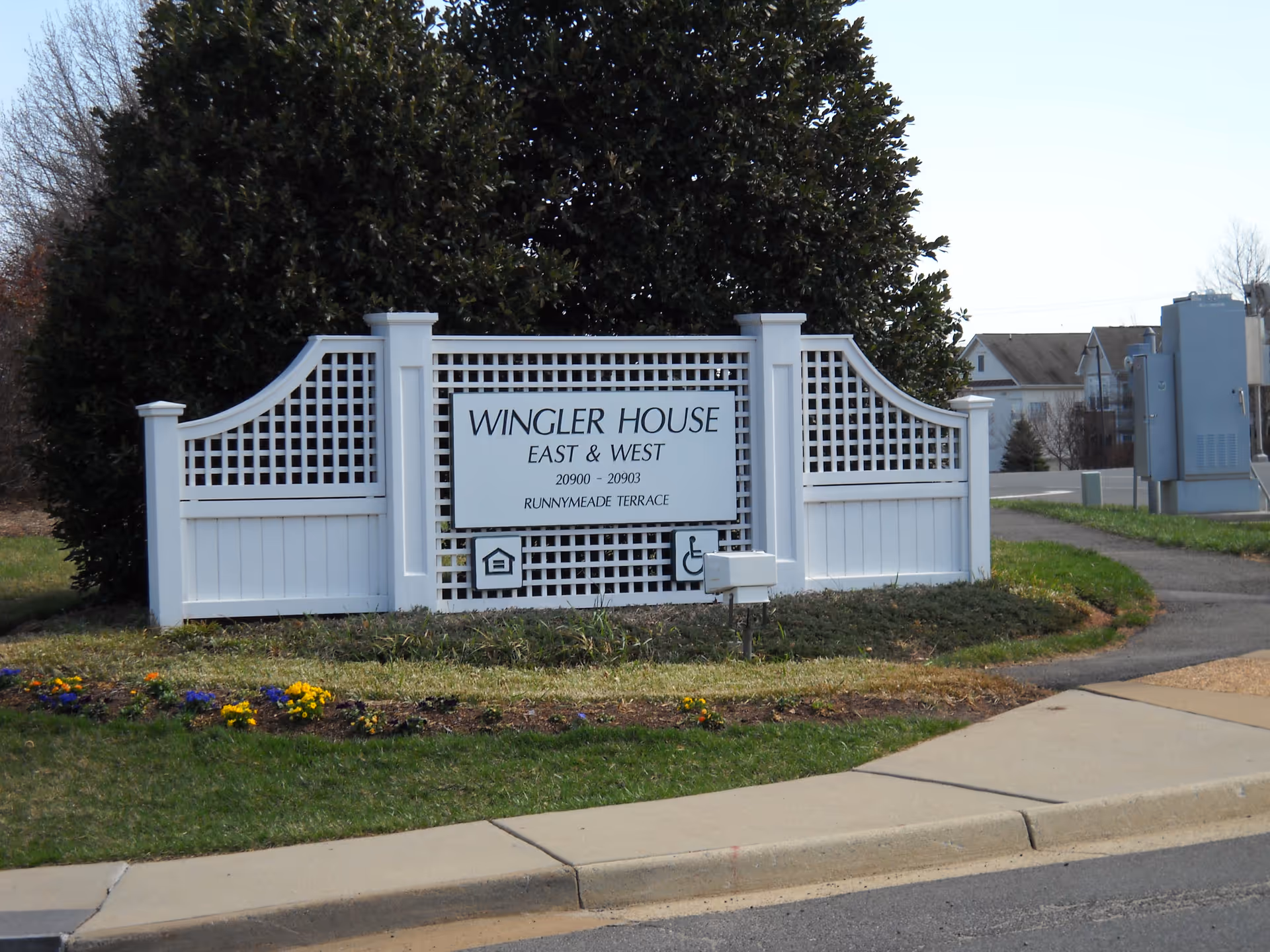 White lattice gate frames a sign for Wingler House, East & West.