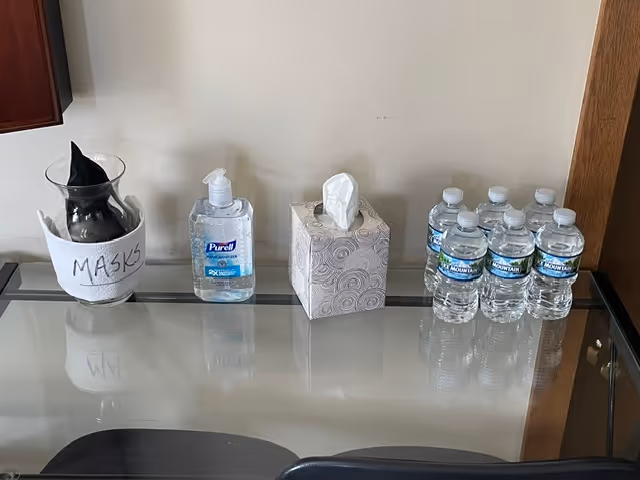 A glass counter holds masks, hand sanitizer, a tissue box, and bottled water.