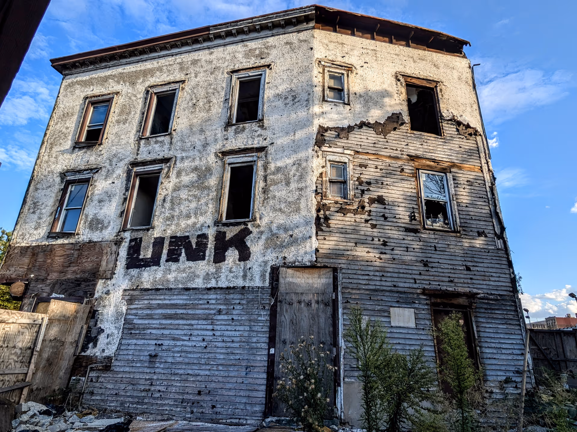 Dilapidated, partially burned three-story building with peeling siding and broken windows.