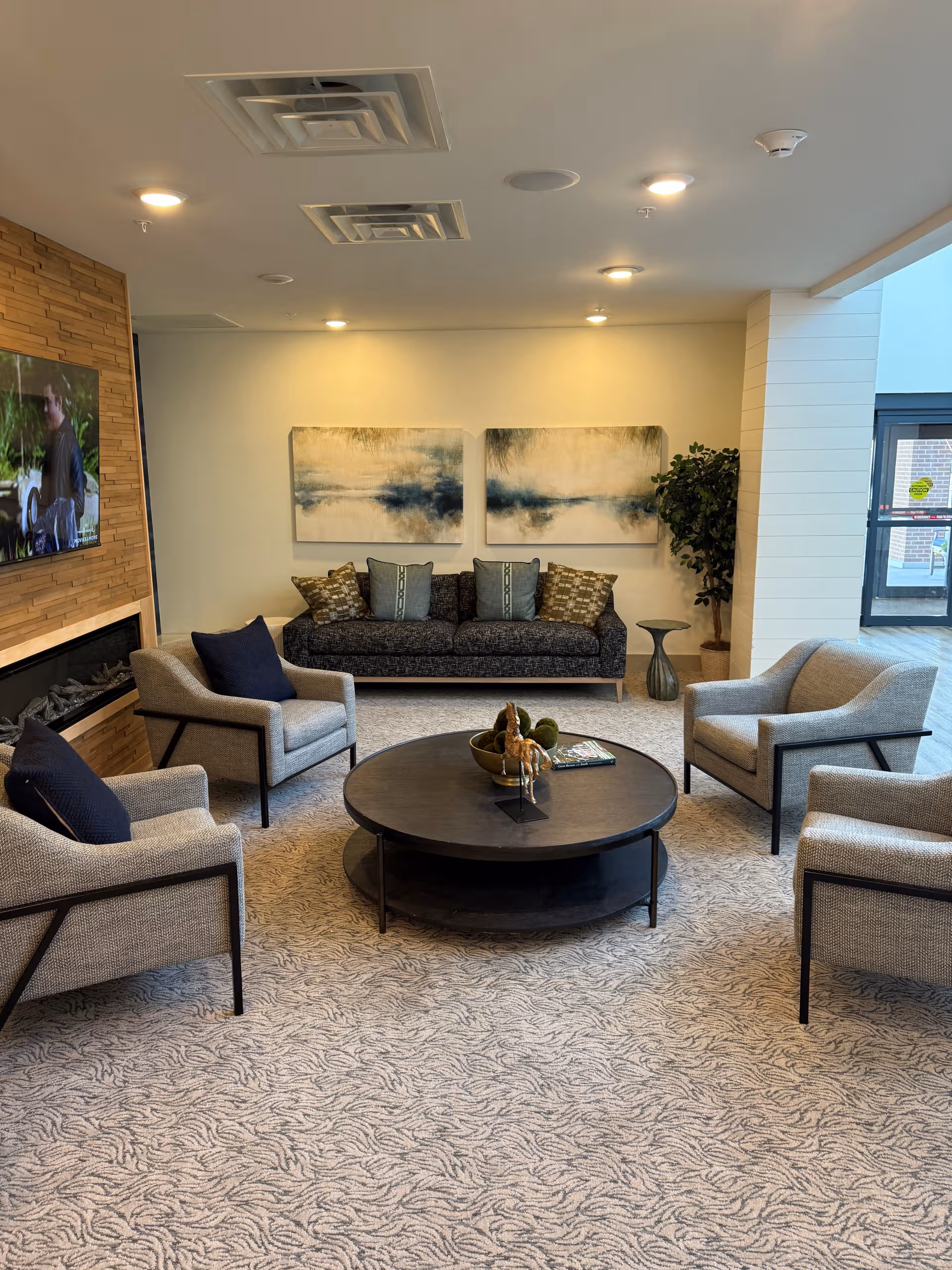 A modern senior living lounge with circular coffee table, surrounding armchairs, and a sofa.