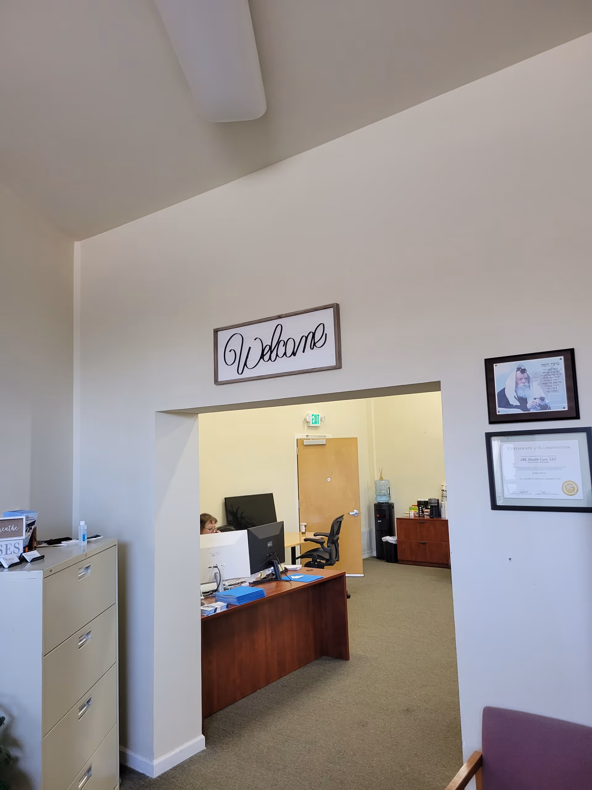 Reception area with a 'Welcome' sign, desk, computers, and doorway to offices.