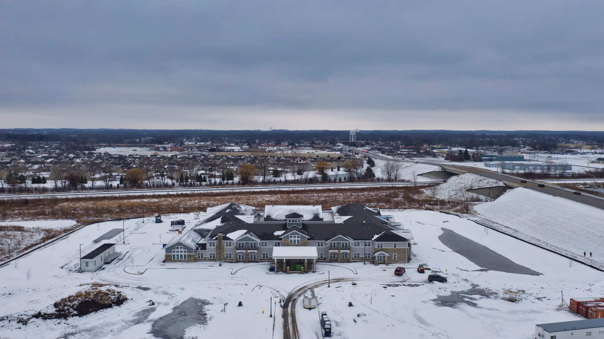 Aerial view of a snow-covered Cedarhurst senior living facility with surrounding roads and parking.