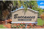Entrance sign reading Buccaneer 55+ Community with palm trees and landscaping.