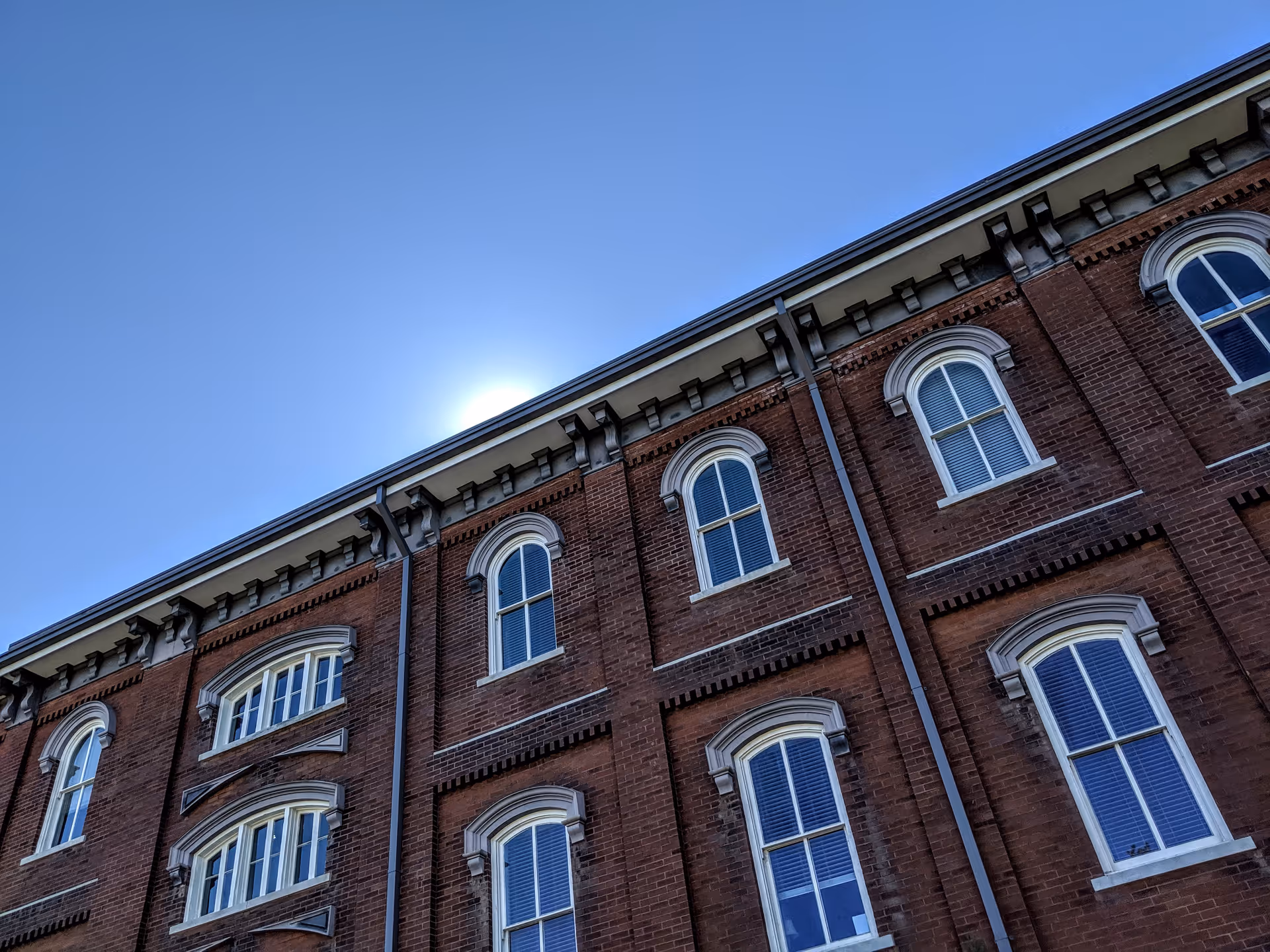 Low-angle view of a brick building facade with arched windows against a clear blue sky.