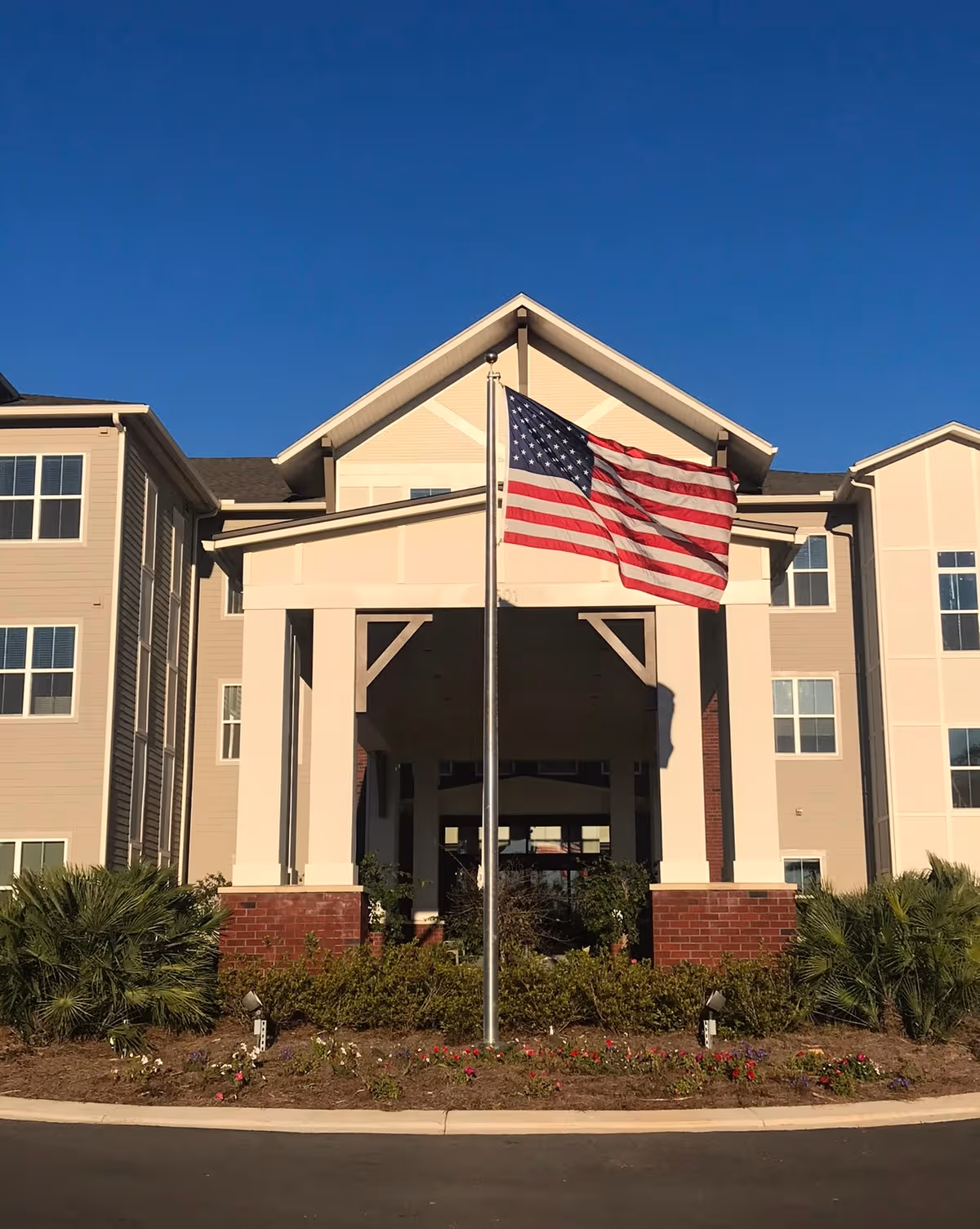 Front view of The Grove at Trelago entrance with American flag and landscaped shrubs.