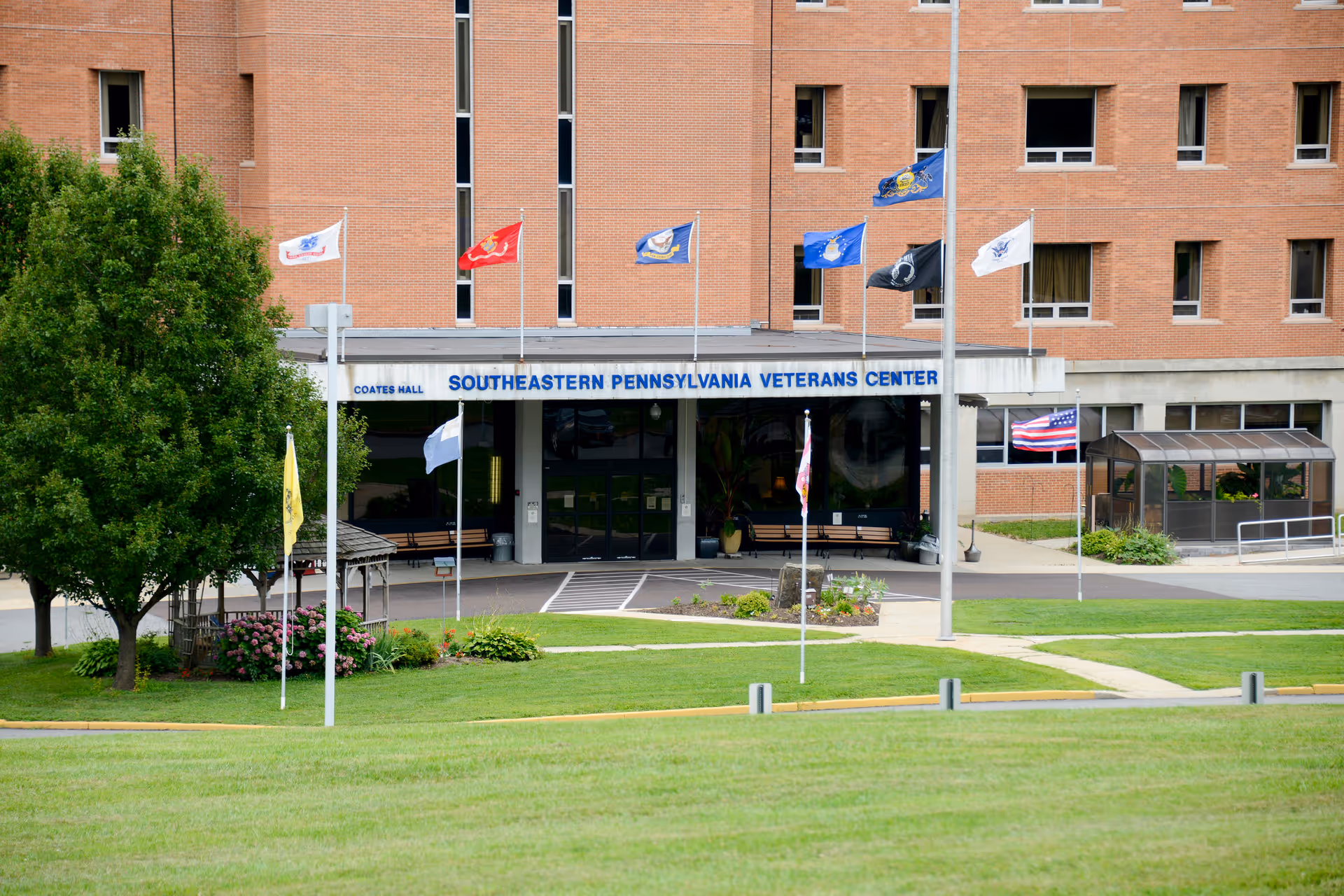 Brick facade and main entrance of the Southeastern Pennsylvania Veterans Center with multiple flags and a manicured lawn in front.