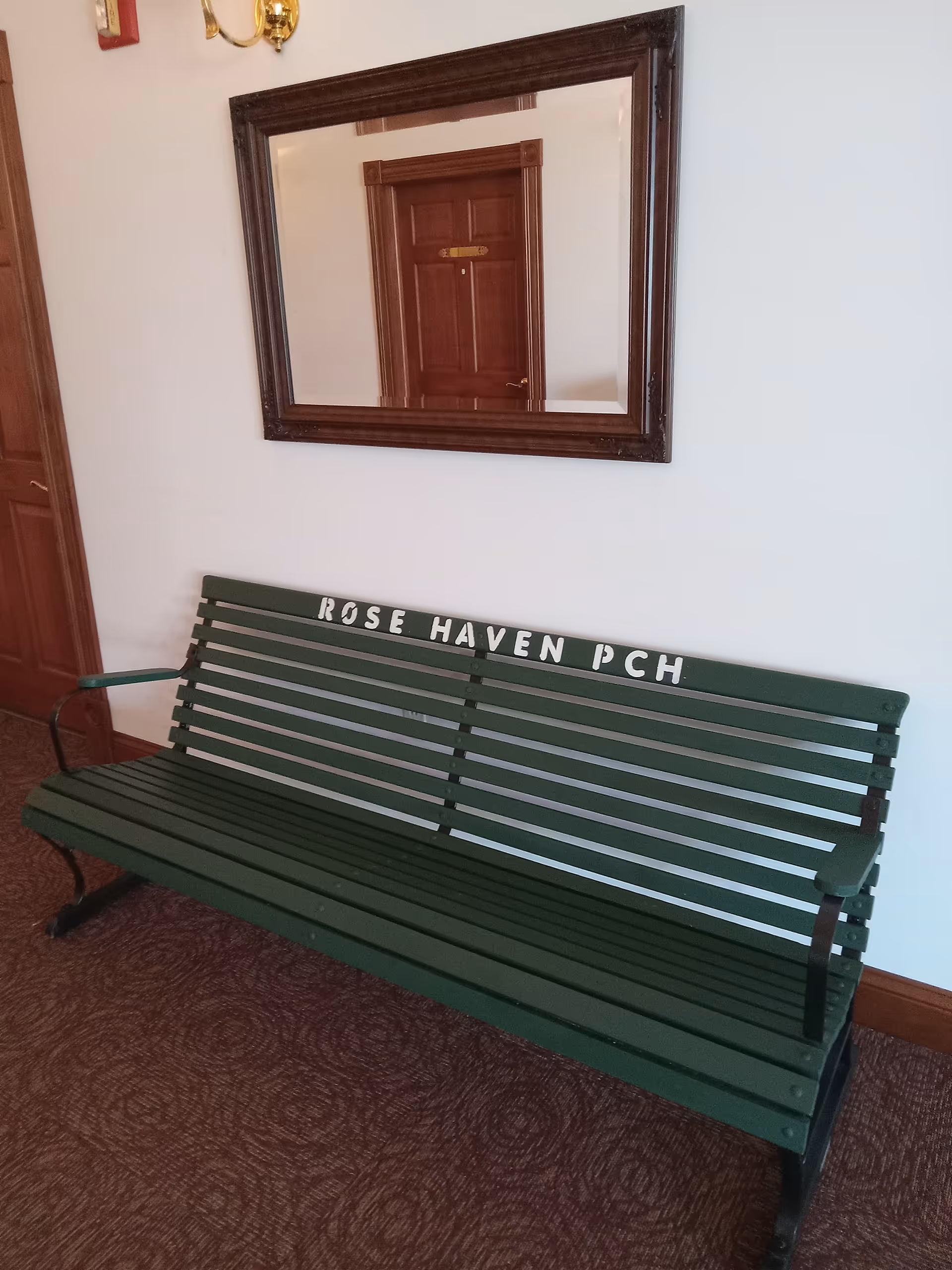 Green bench with Rose Haven PCH lettering sits in a hallway beneath a framed mirror.