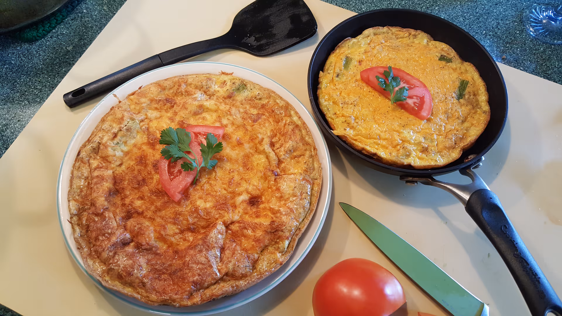 Two frying pans with omelets and a tomato garnish on a kitchen counter.
