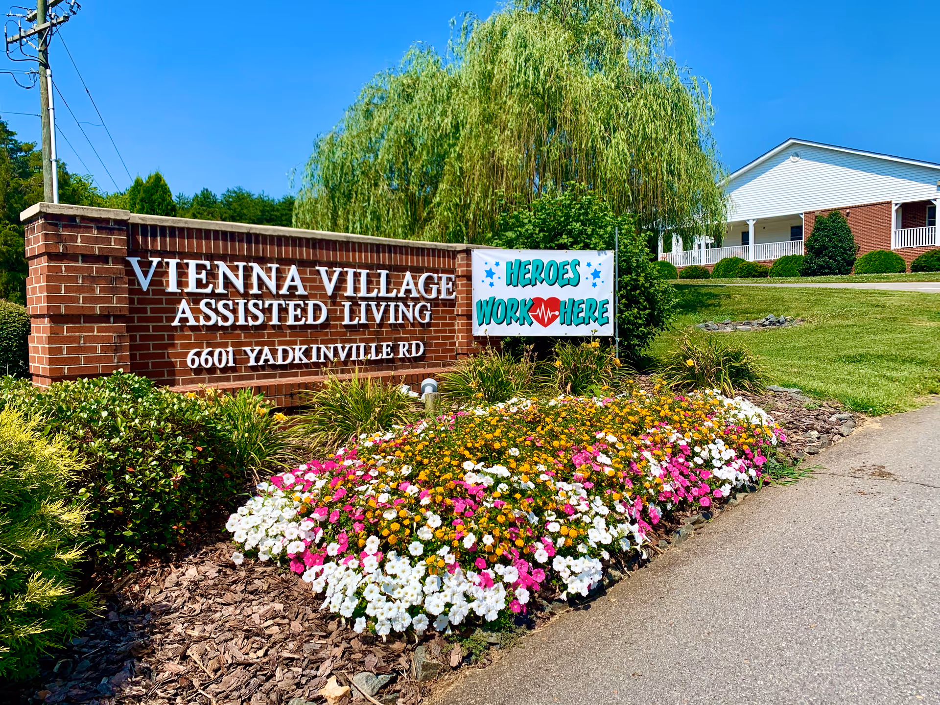 Brick sign reads Vienna Village Assisted Living with colorful flowers and a banner.
