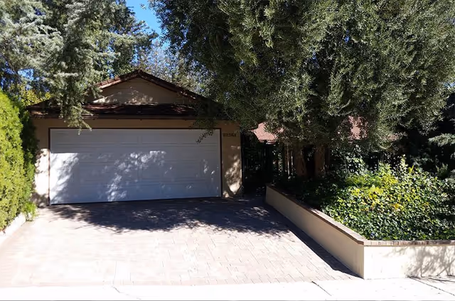 Front view of Villa Mulholland II with a closed garage, paved driveway, and surrounding trees.