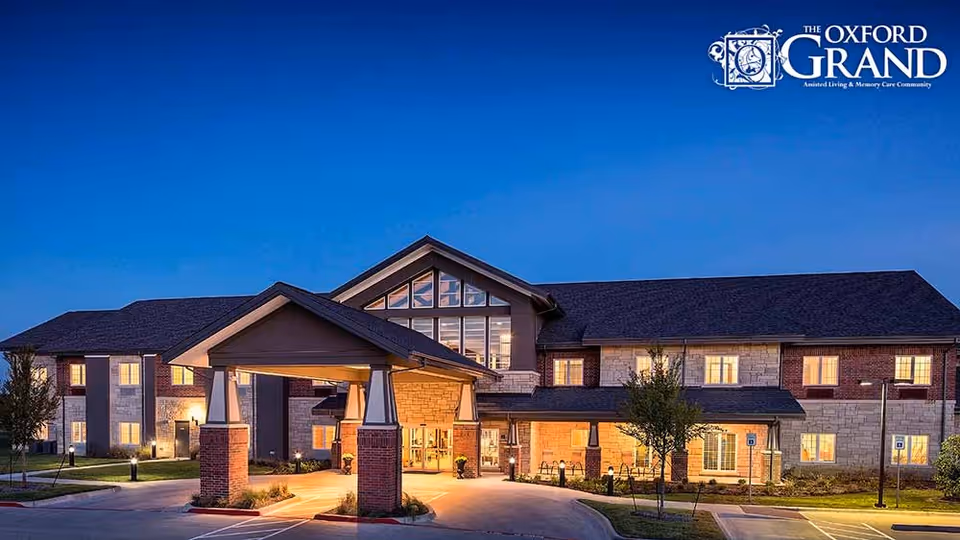 Front entrance of The Oxford Grand assisted living facility at dusk with lit windows and a covered porte-cochère.