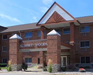 Brick multi-story senior living building entrance with a covered porte-cochère and the sign 'SUMMIT WOODS' above the entry.