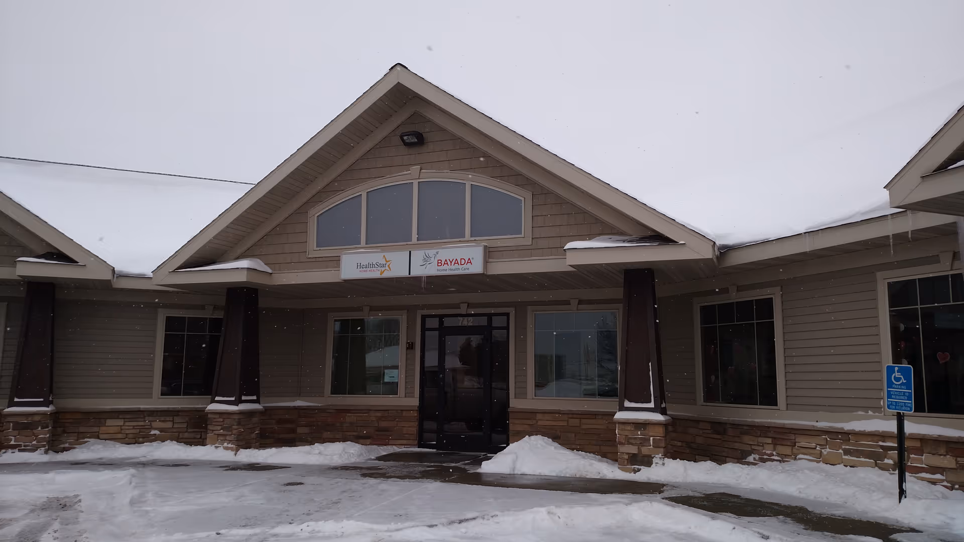 Snowy front of a senior living facility with entrance and signage.