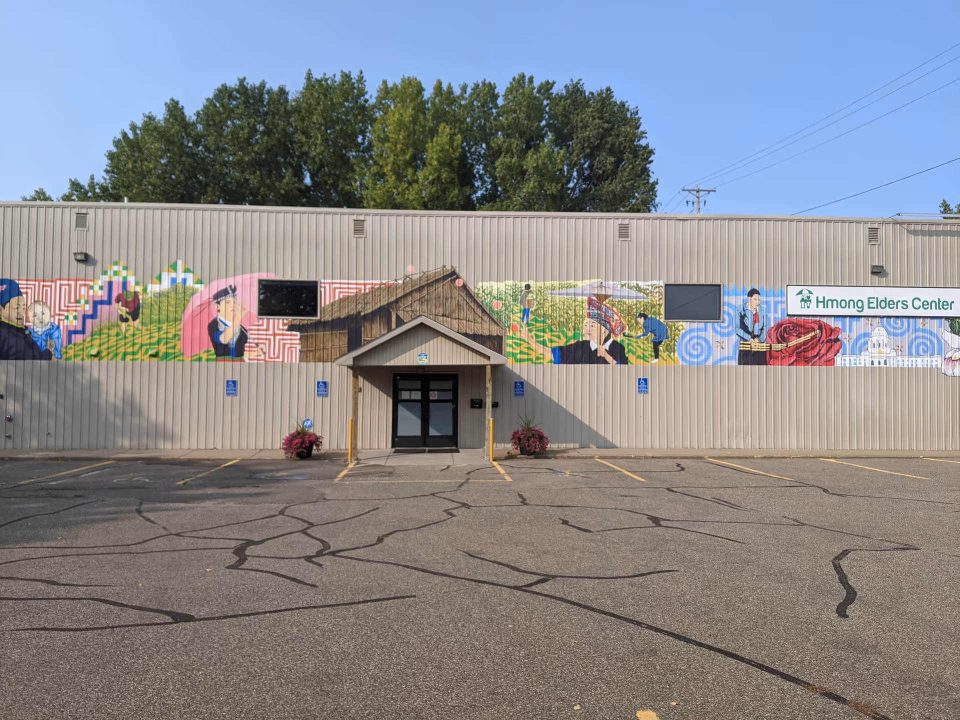Exterior view of a beige building with a colorful mural and Hmong Elders Center sign.