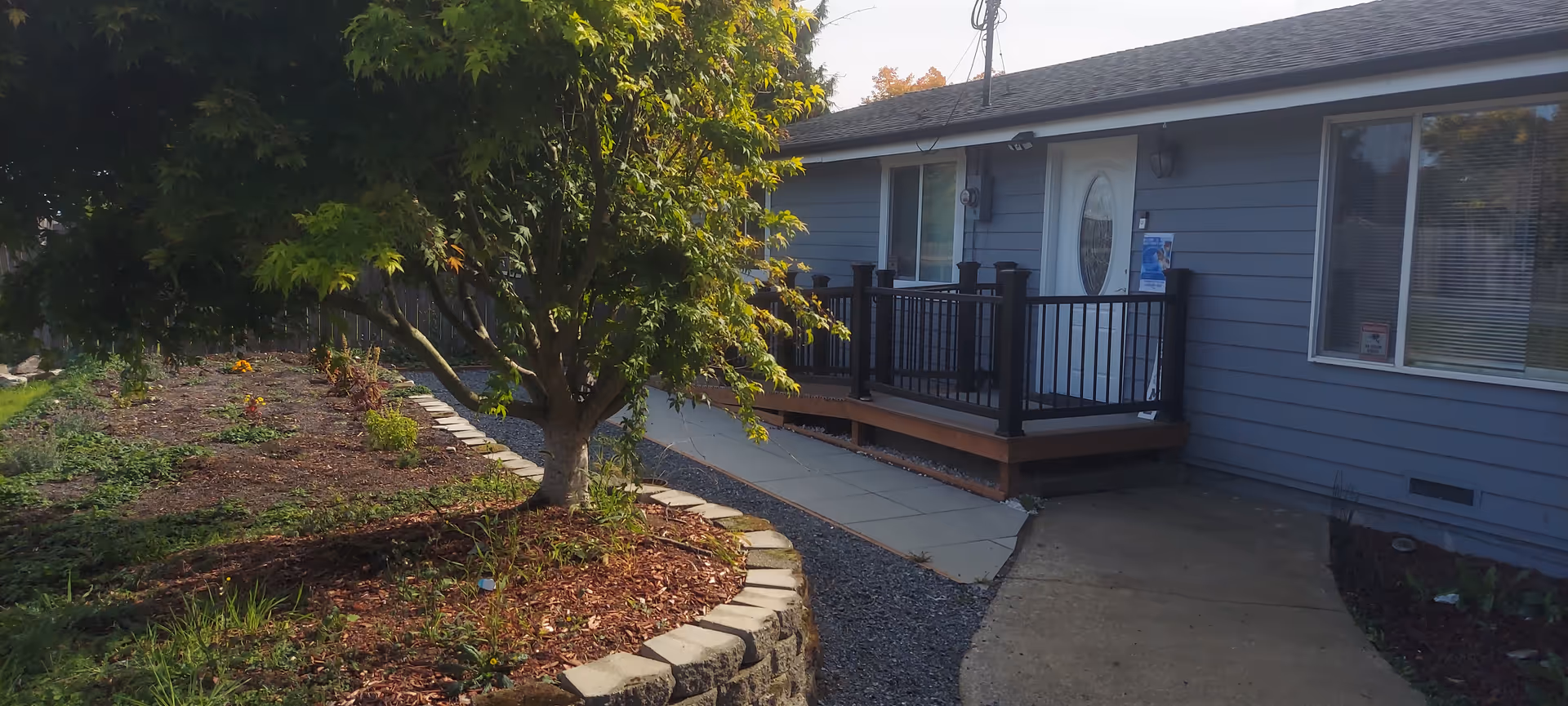 Blue single-story senior living home exterior with a deck, walkway, and garden.