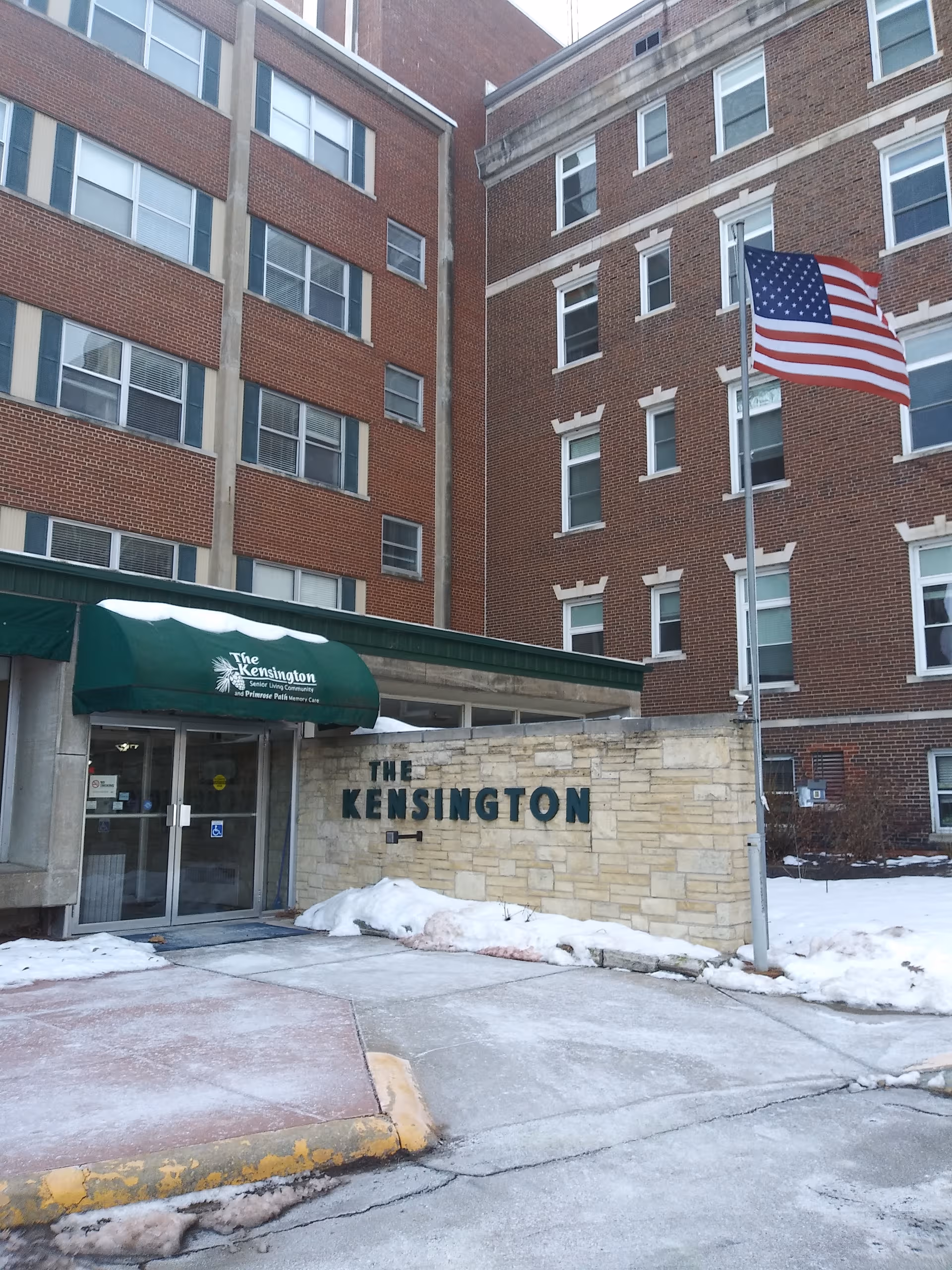 Front view of The Kensington Fort Madison entrance with an American flag and stone sign.