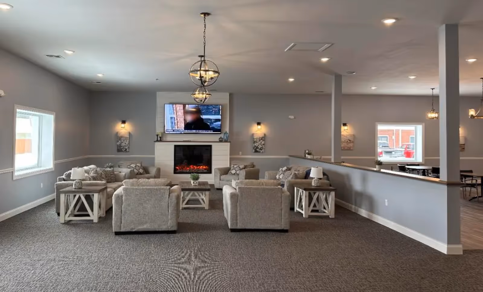 North Branch Assisted Living lounge with gray seating, tables, a fireplace, and a mounted TV.