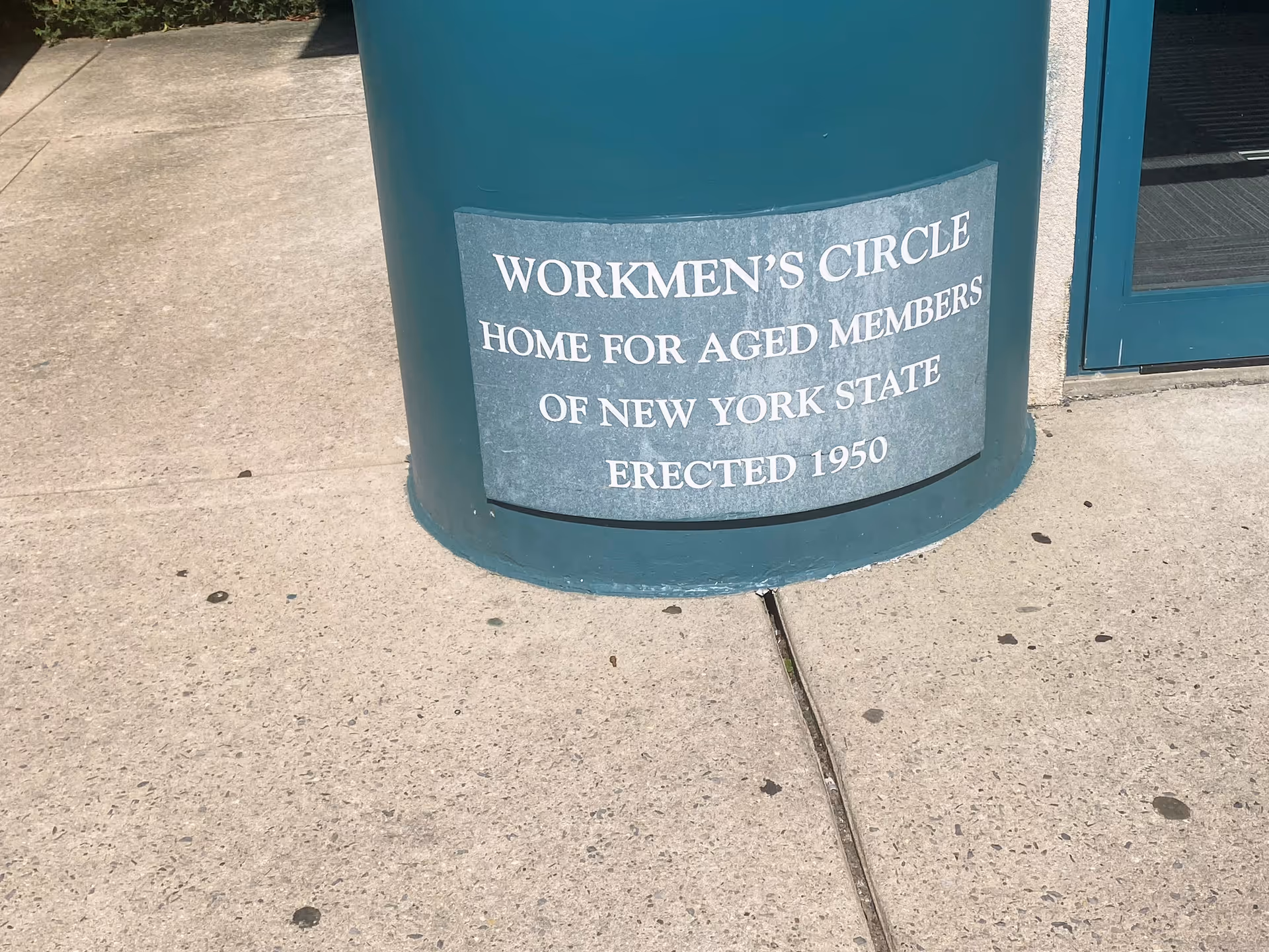 Teal exterior column plaque reads 'Workmen's Circle Home for Aged Members' outside.