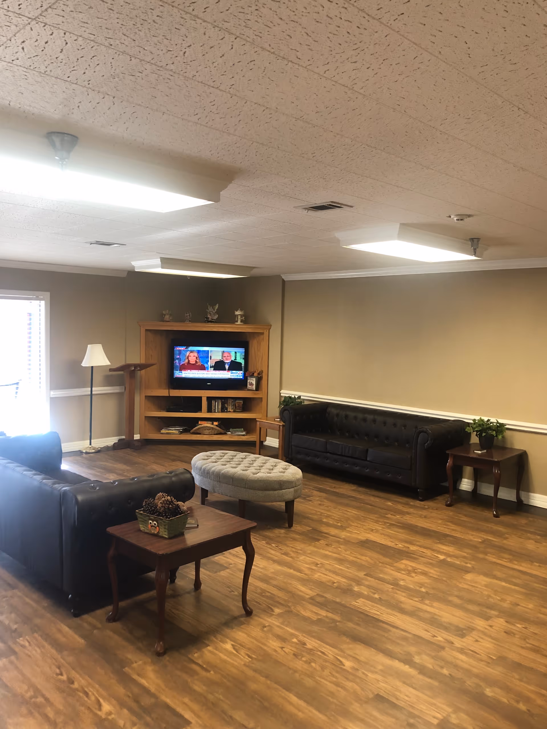 A cozy senior living lounge with leather sofas, ottoman, coffee tables, and TV.