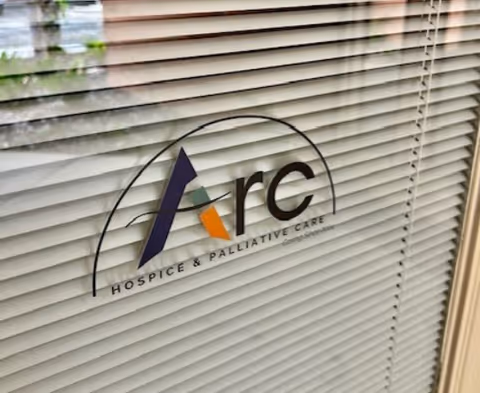 ARC Hospice logo on glass with horizontal blinds in foreground.
