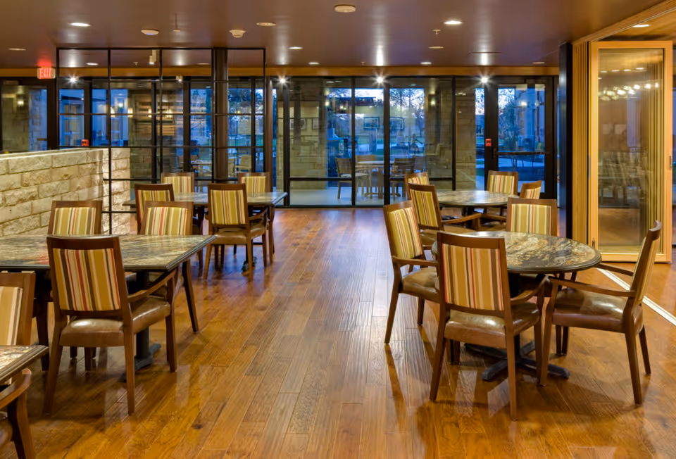 Elan Southpark Meadows dining area with wooden tables, striped chairs, and glass walls.