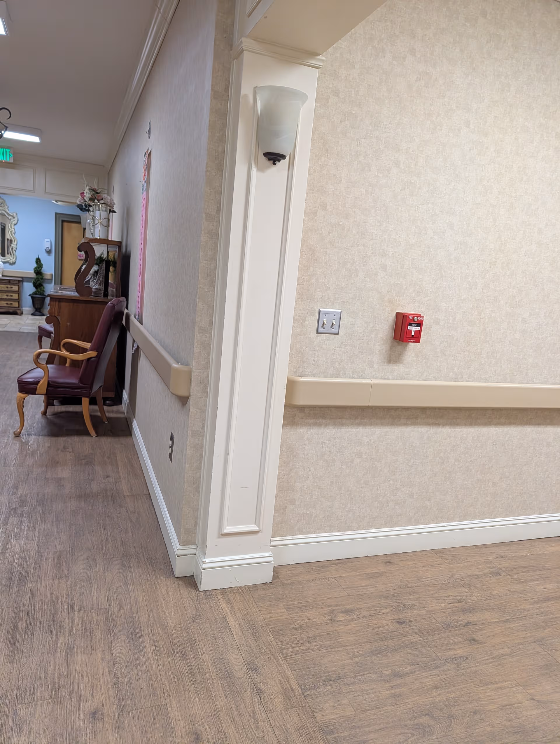 Hallway inside Chapman Health Care-Assisted with wooden floor, chairs, and decorative furnishings.