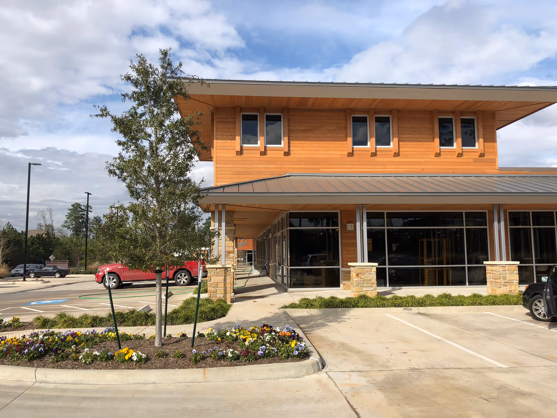 Wooden-clad medical clinic with large glass doors, stone columns, and landscaped parking.