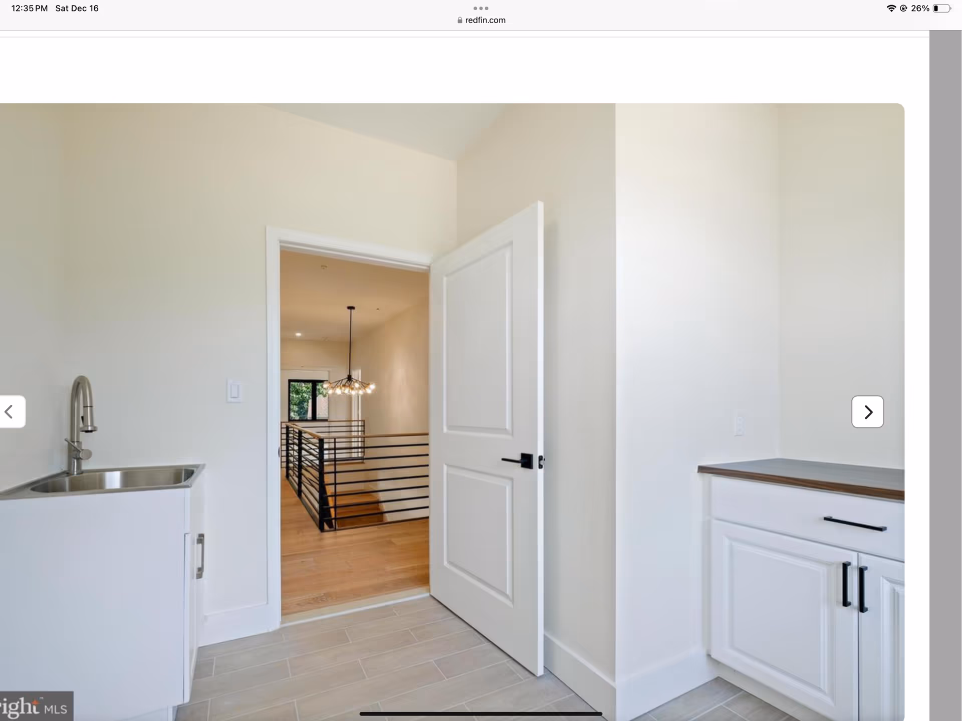 Bright modern kitchen area with sink, cabinets, doorway to hallway and railing visible beyond