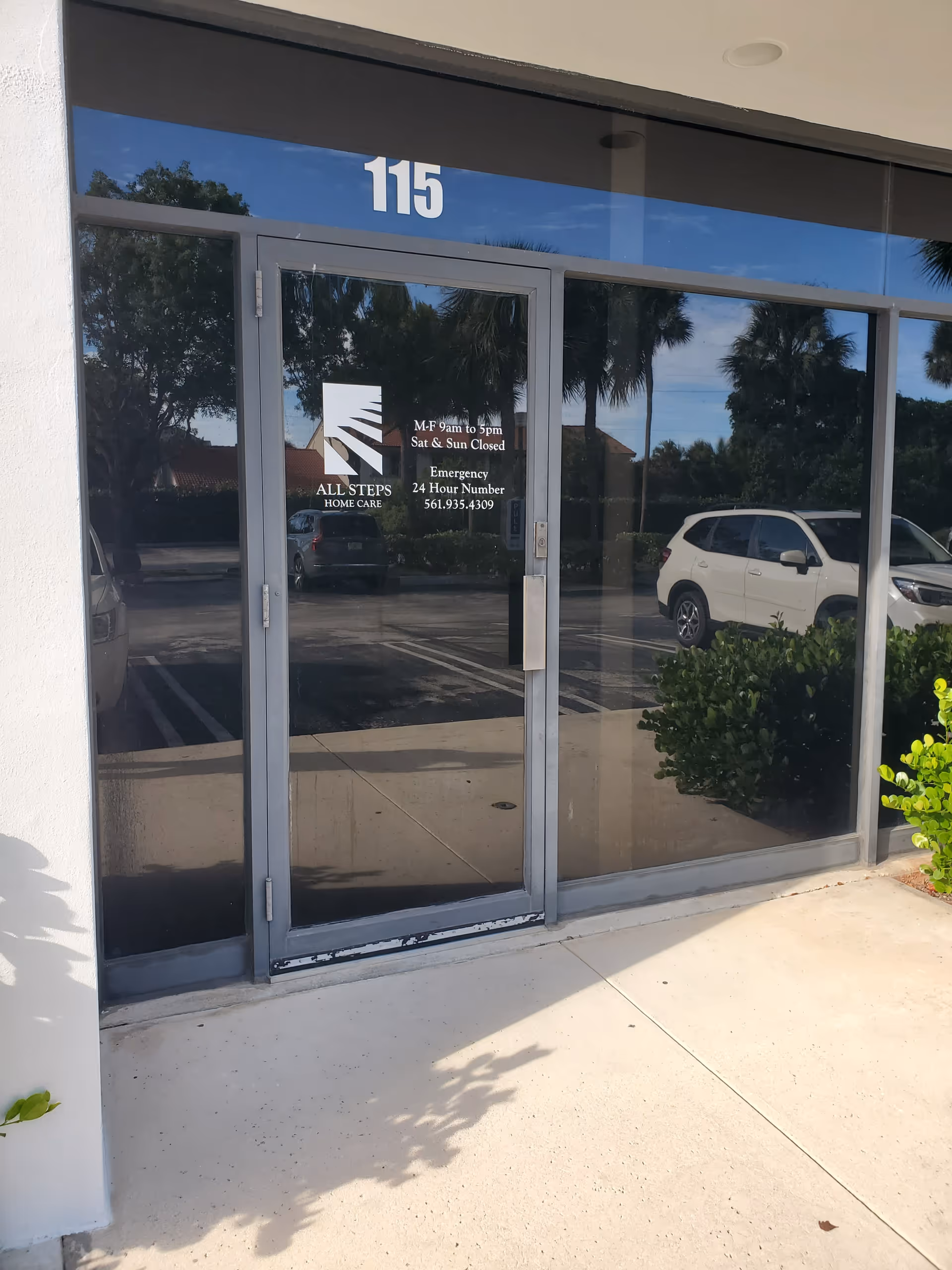 Glass entrance door displaying All Steps Home Care logo, address 115, with reflected parking lot.