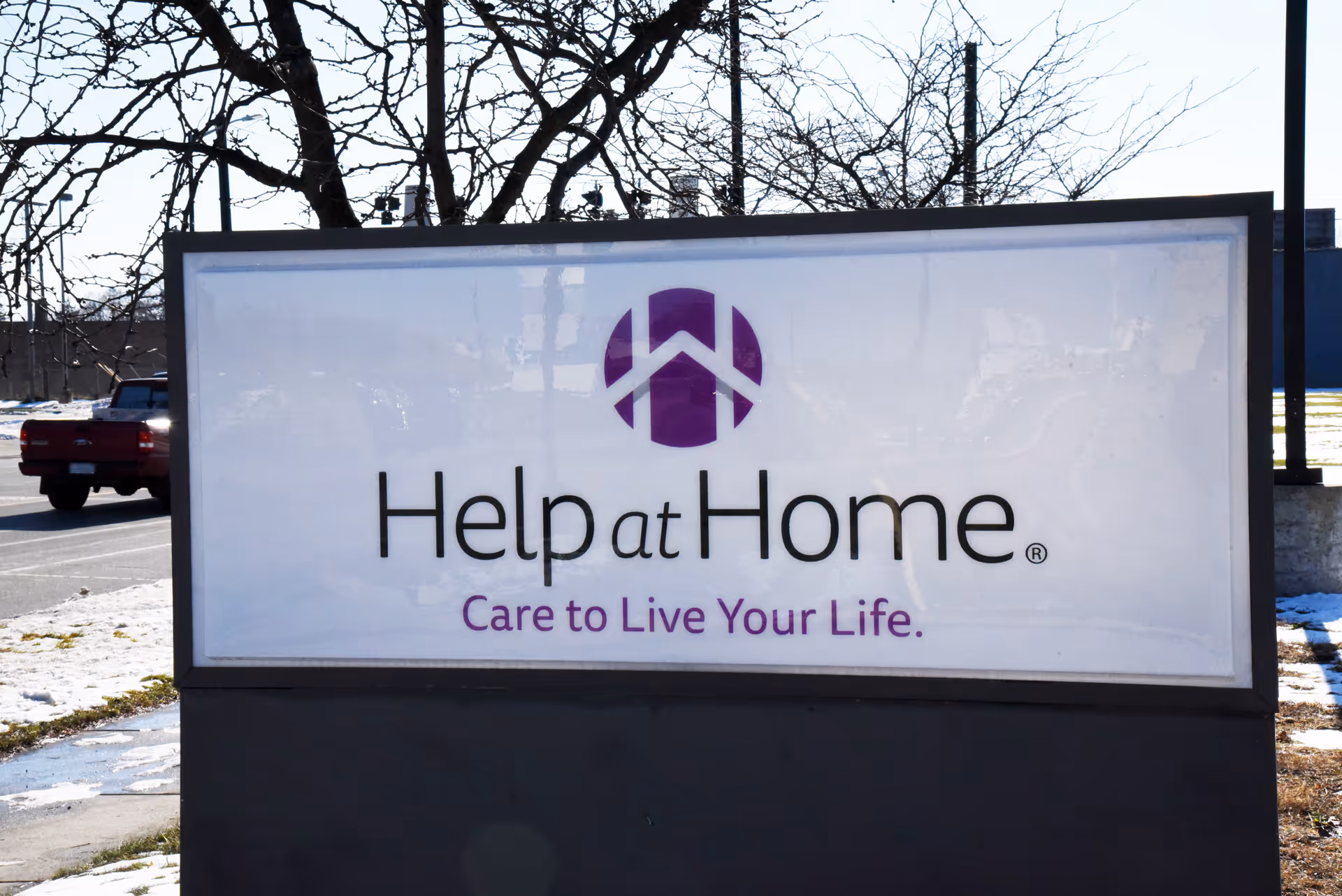 A large Help at Home sign with logo and slogan in a parking lot.
