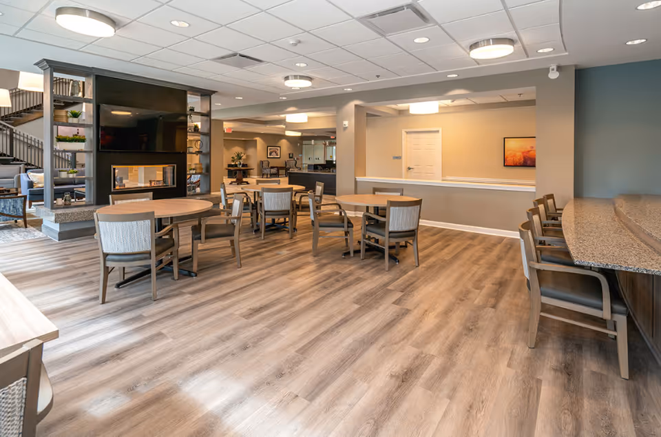 Spacious senior living common area with round tables, chairs, and a long service counter.