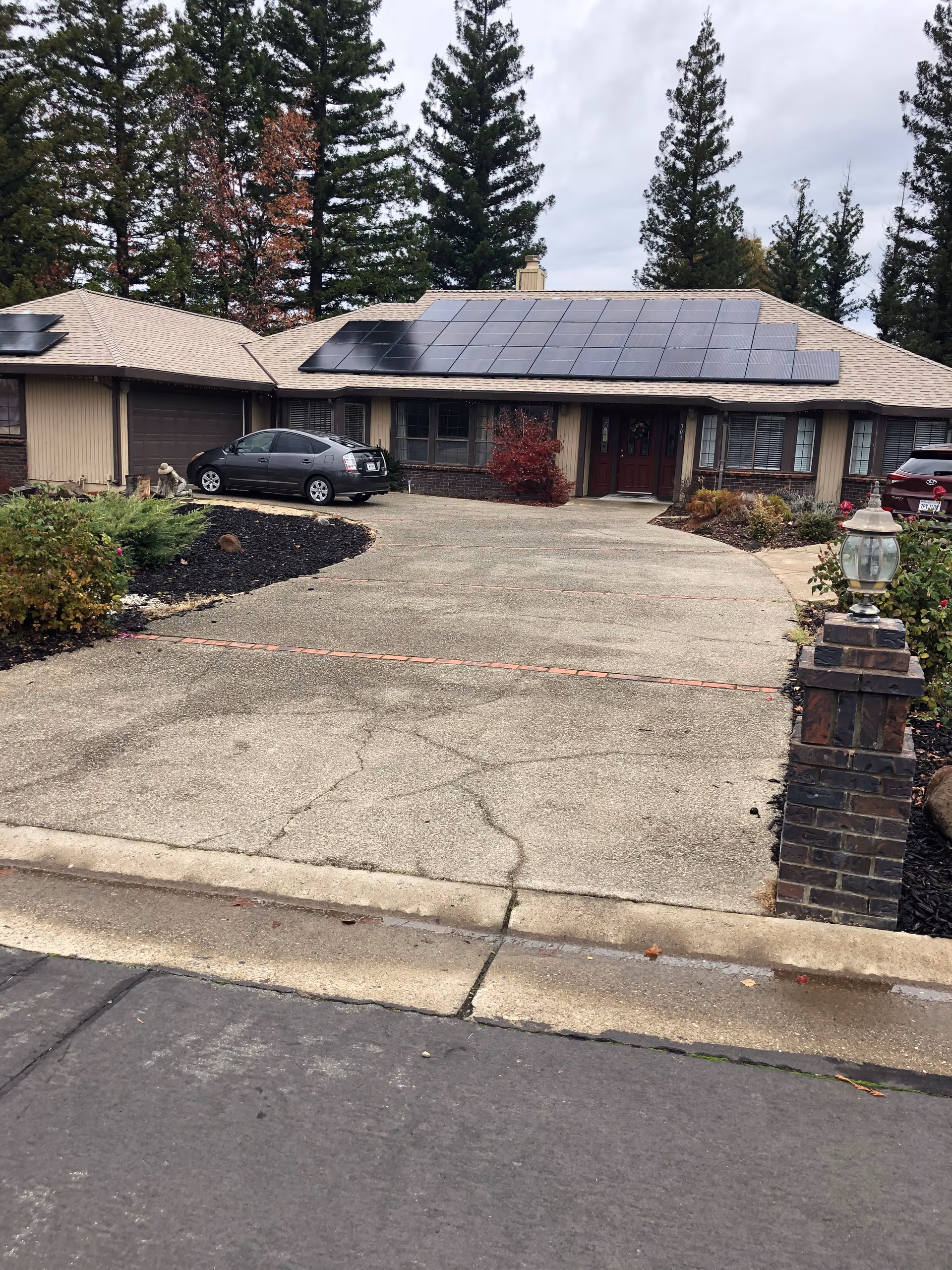 Front exterior of a single-story residence with solar panels and parked cars.