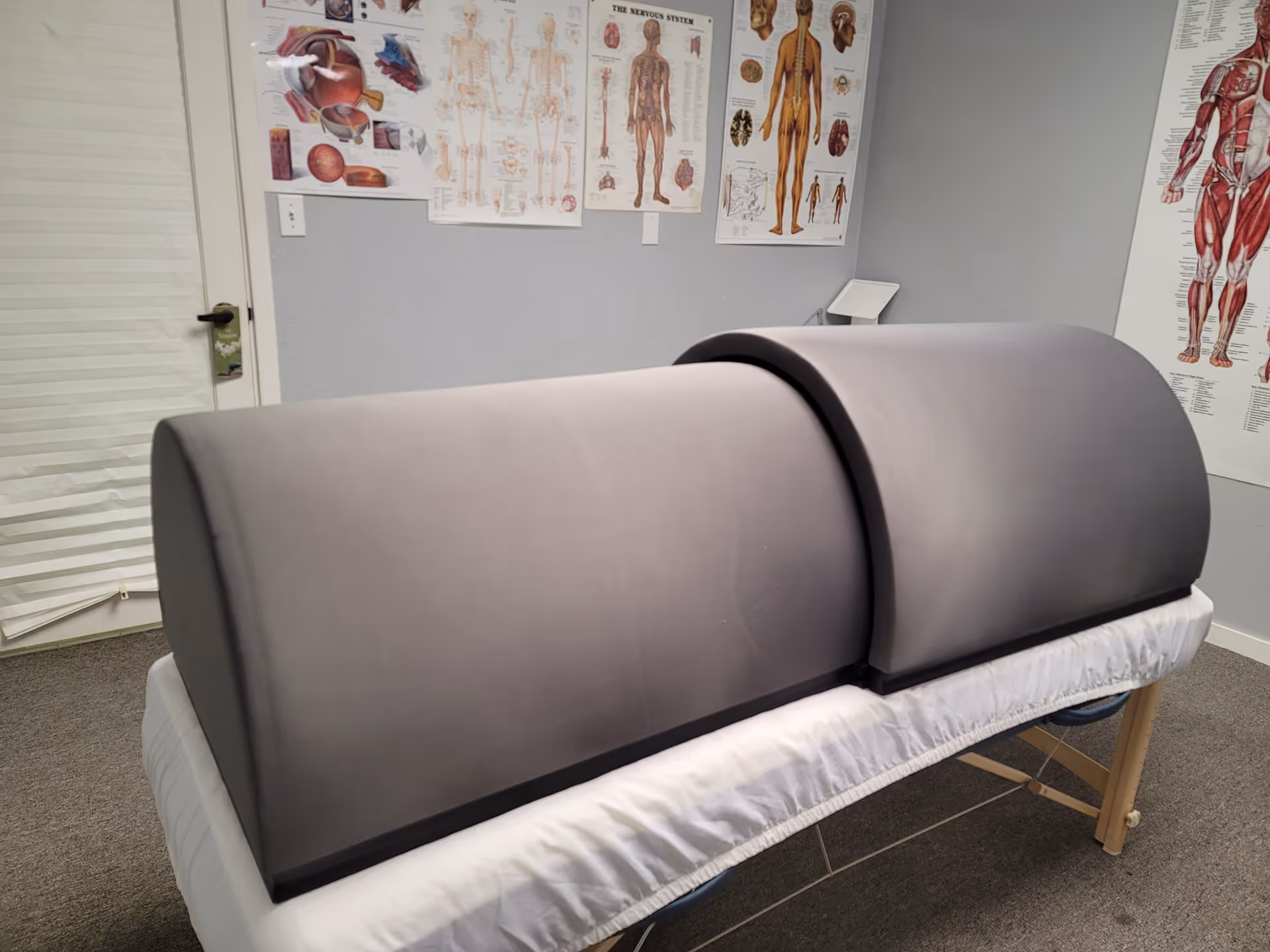 A padded massage/exam table in a treatment room with anatomy charts on the walls.