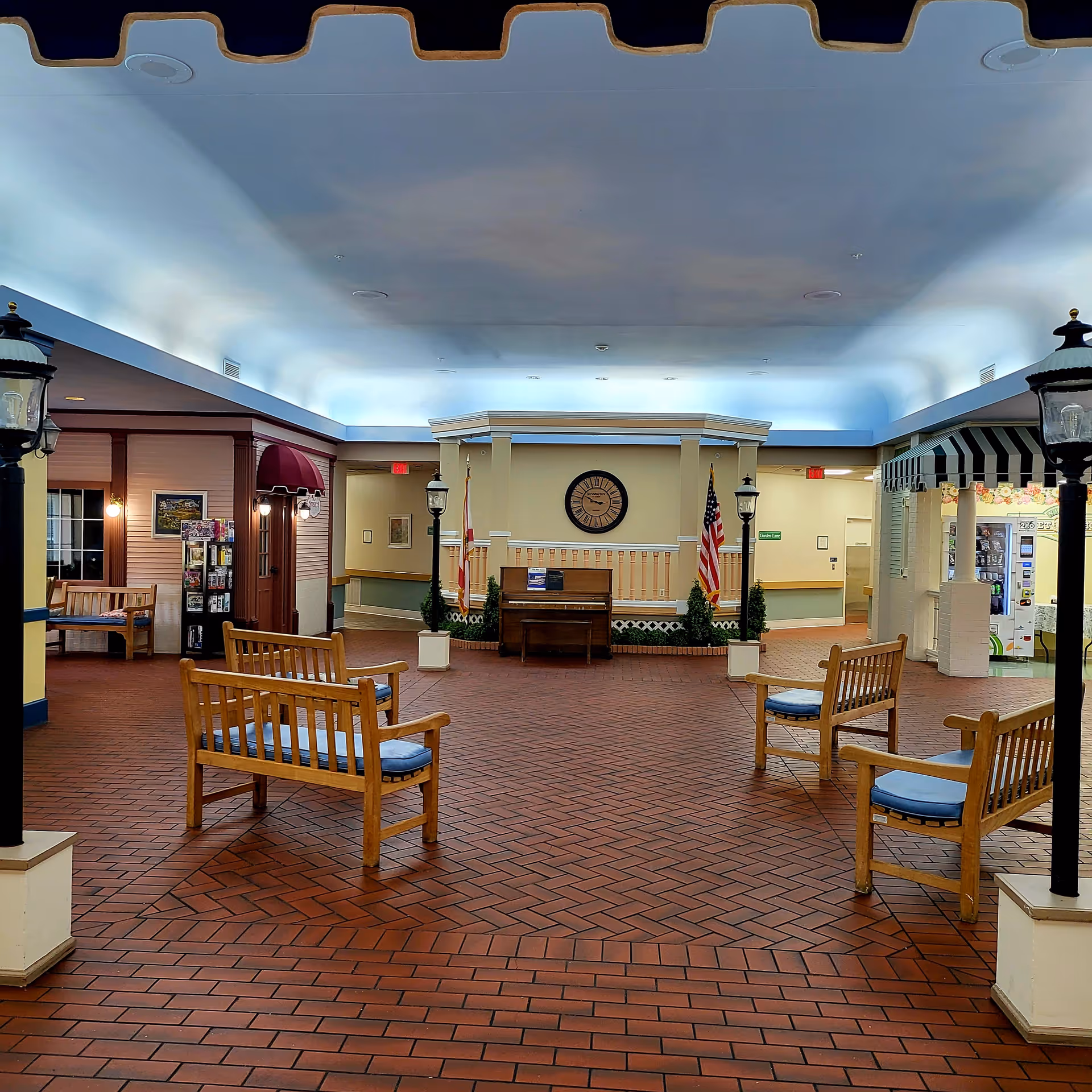 Indoor atrium-style lobby with brick floor, seating, flags, clock, and vending area.