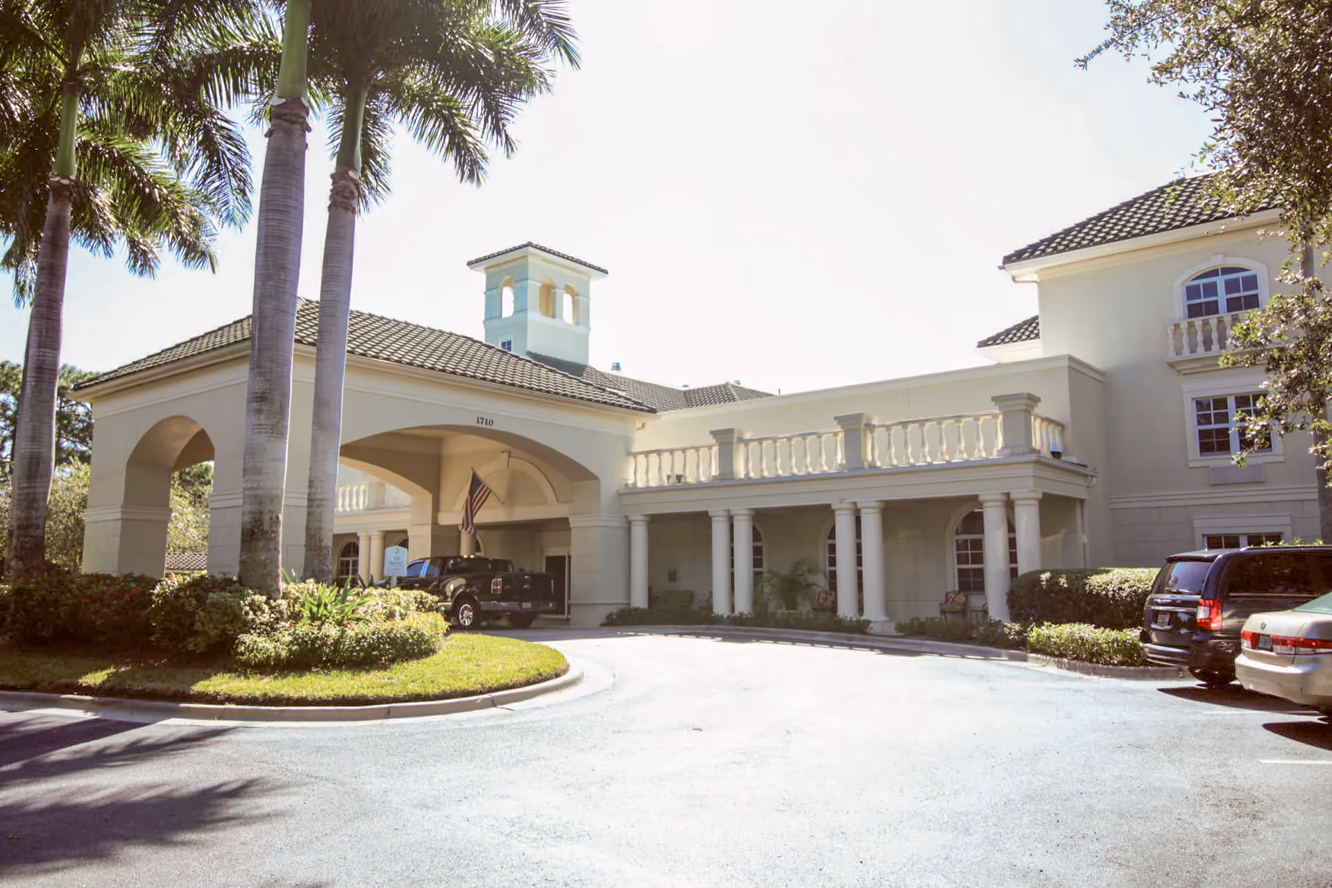 Cream-colored senior living building with arches, columns, and palm trees at a circular driveway.