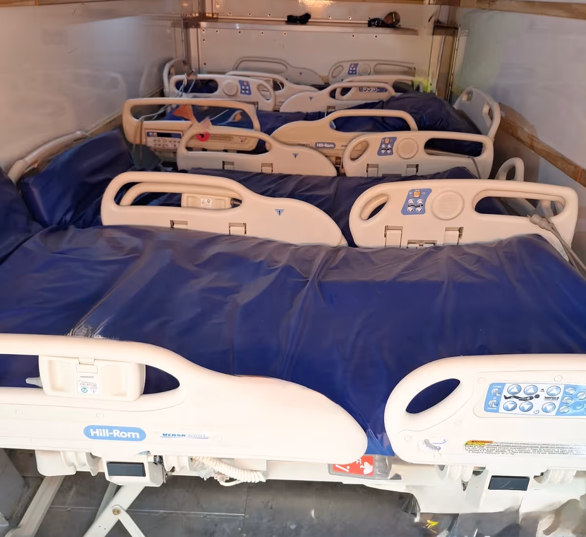Interior storage area with multiple hospital beds covered in blue bedding arranged in rows.