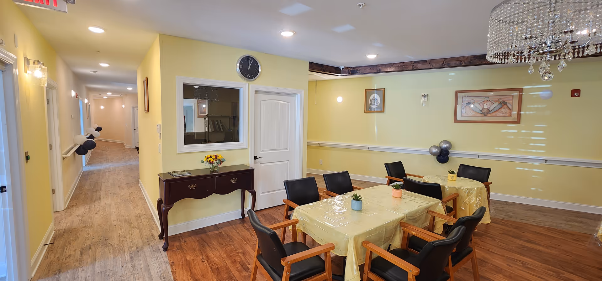 Yellow-walled dining area with tables, chairs, a chandelier, and a hallway.