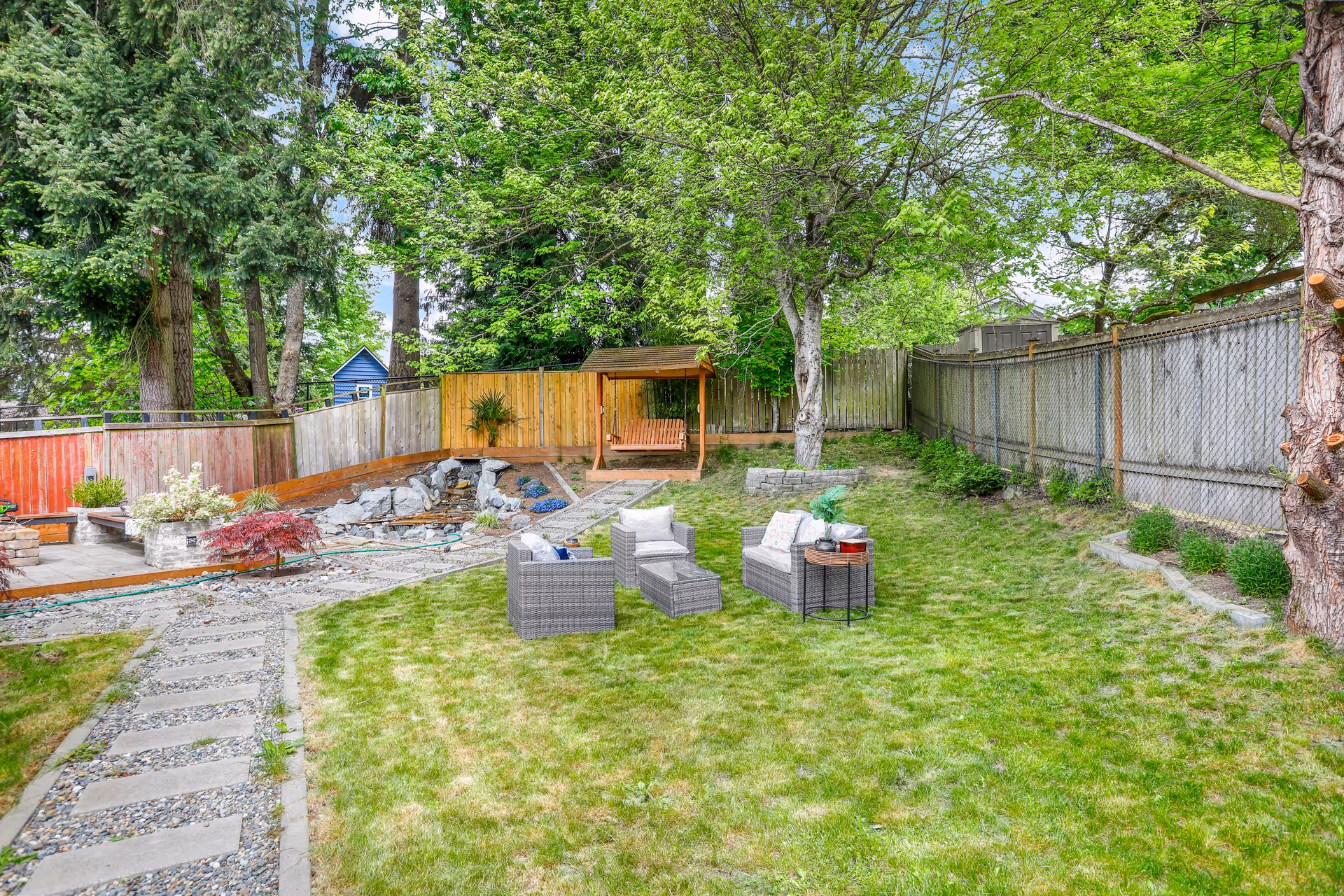 Fenced backyard with trees, grass, and outdoor seating.