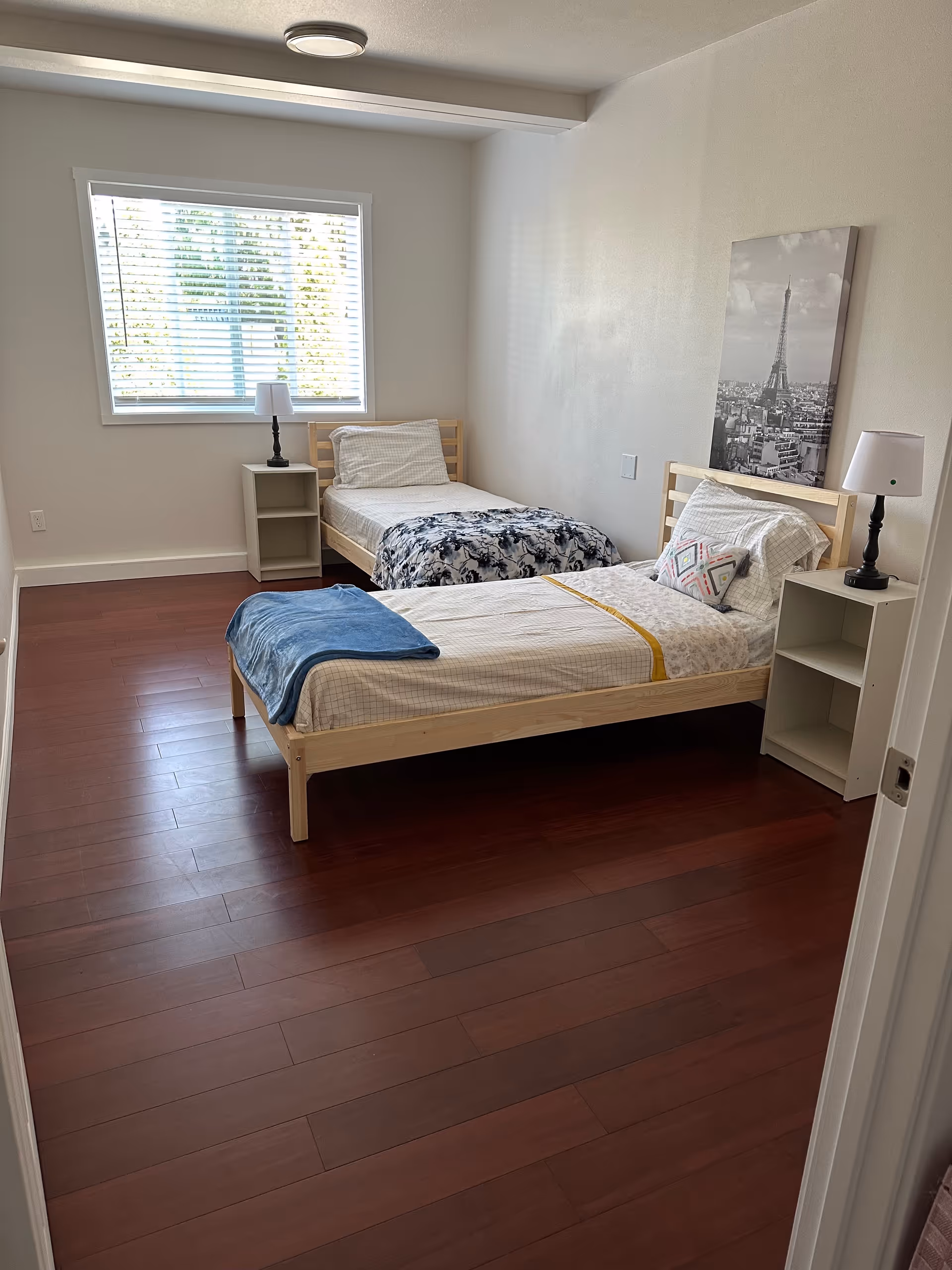Two single beds in a bright shared bedroom with nightstands and Eiffel Tower artwork.