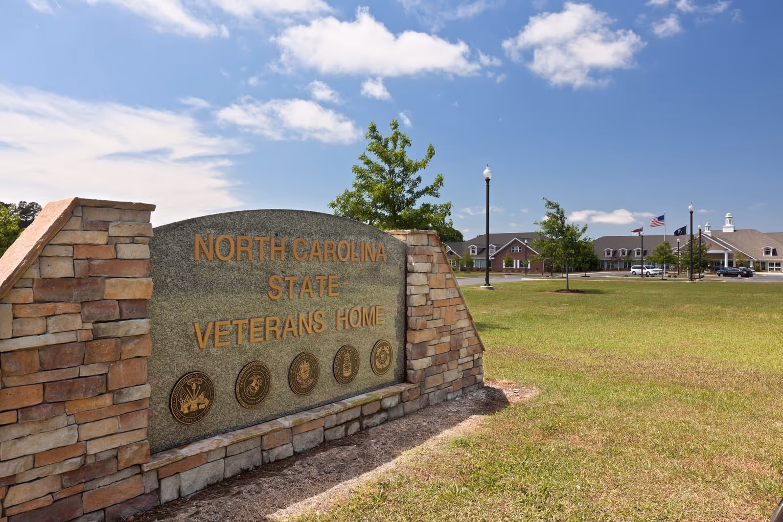 Stone sign reads North Carolina State Veterans Home with lawn and distant building.