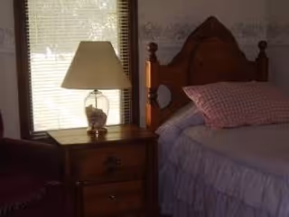 Bedroom with a wooden headboard bed, pink pillows, purple bedspread, and a lamp on a nightstand.