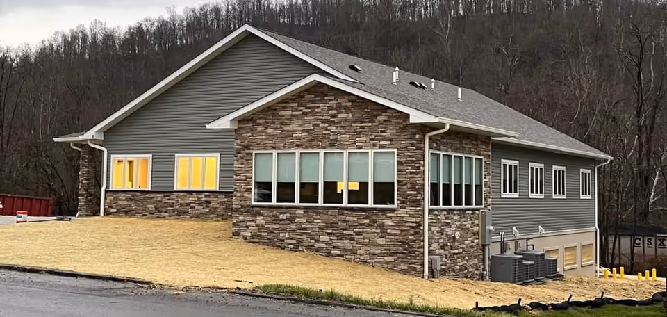 Modern gray building with stone facade sits on a bare dirt lot.