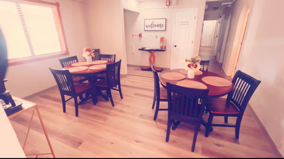 Two round tables with chairs in a bright dining room, hallway visible in background