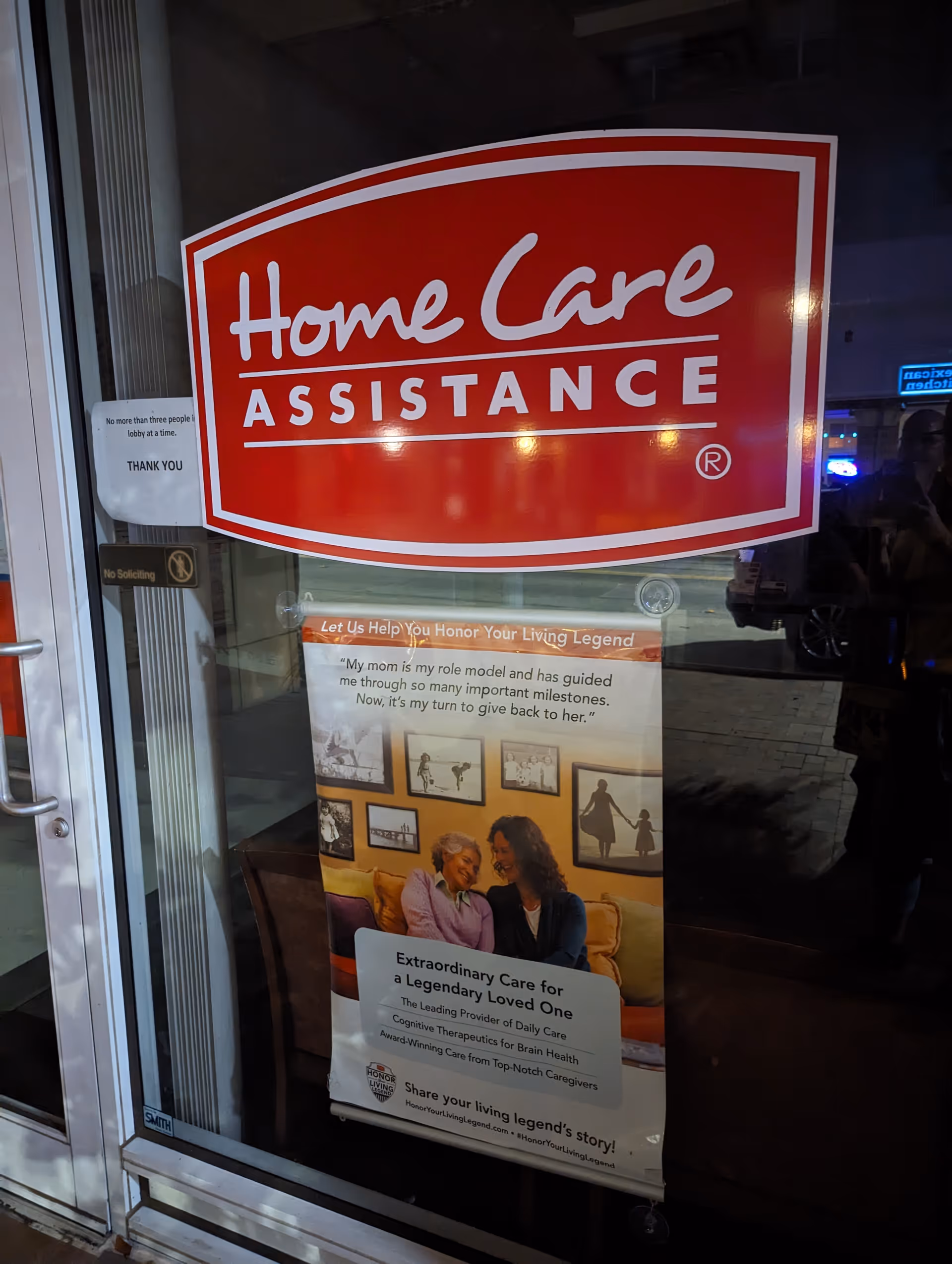 Red Home Care Assistance sign on glass storefront door with a poster below