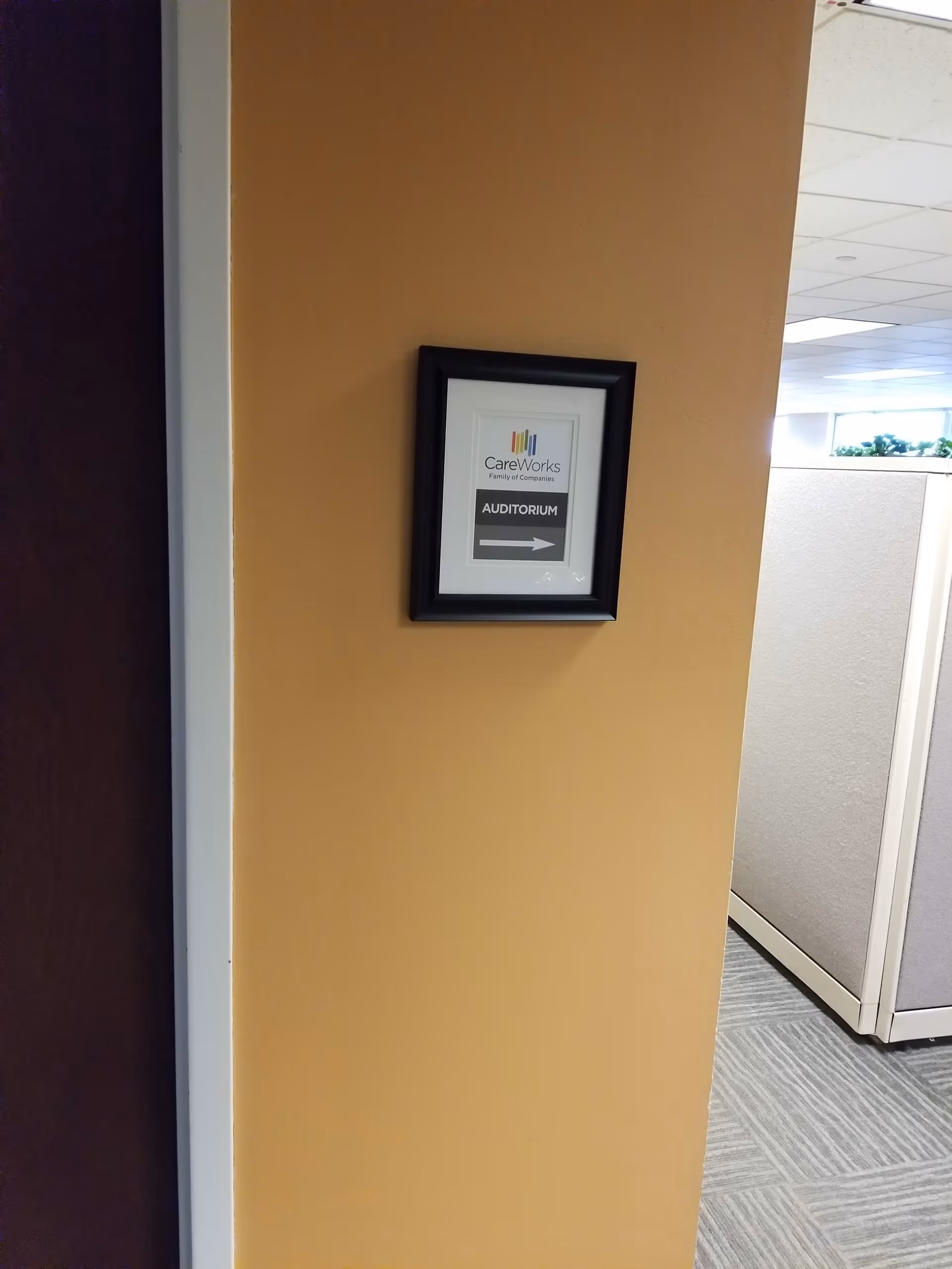 Framed CareWorks sign on orange wall in hallway directs to the auditorium.