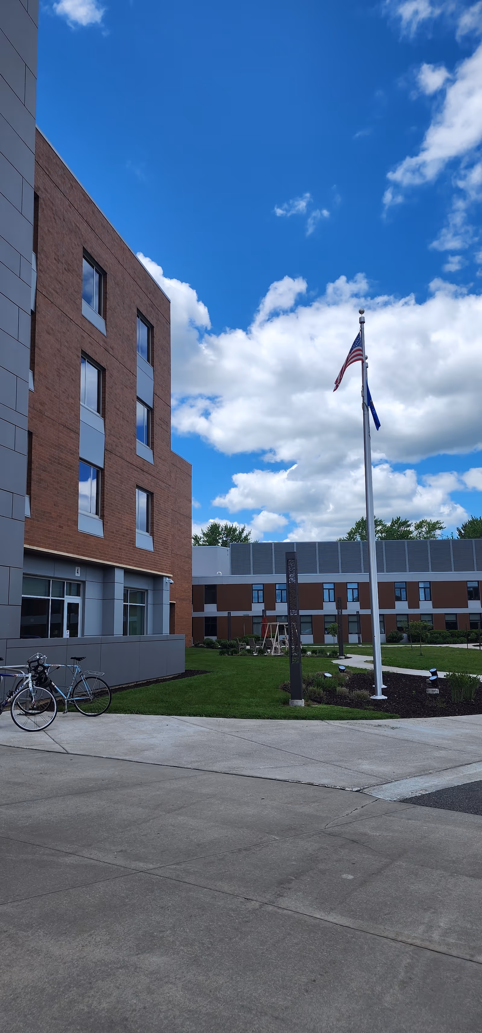 Exterior view of a brick senior living building with flagpole, lawn, and bicycles.