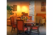 Round dining table with red chairs and a floral centerpiece in a warm lounge area.
