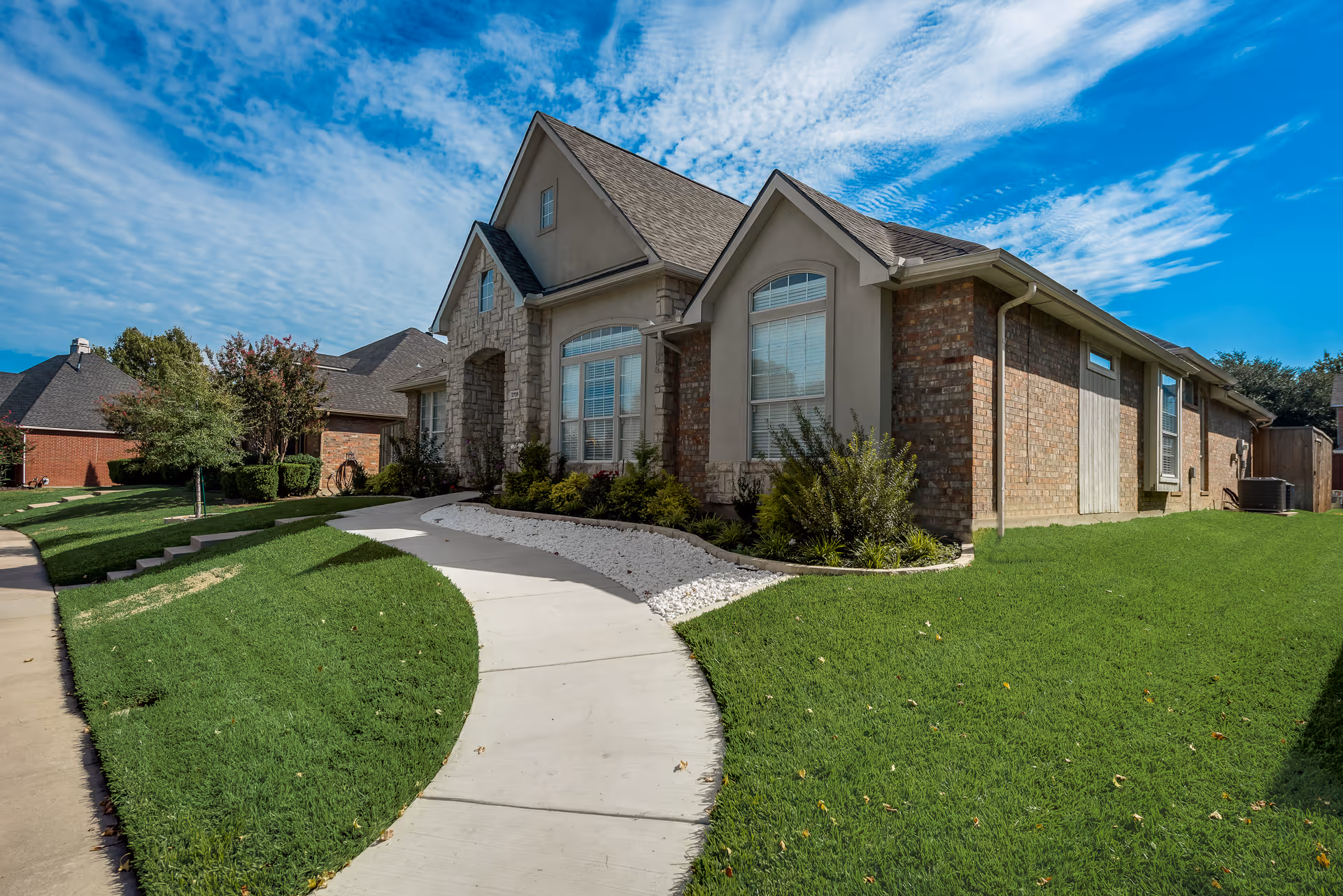 Exterior view of a brick-and-stone senior living home with a curved walkway and green lawn.
